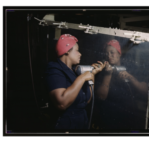 A Black woman, Eugenia Powell Deas, hold a drill to a piece of metal