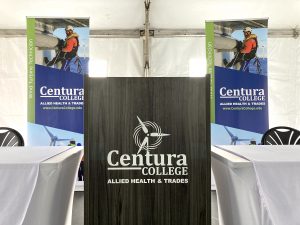 Black podium with Centura College logo incorporated with the image of a Wind Turbine. Two standing posters behind podium show images of a wind turbine technician in safety gear over the ocean