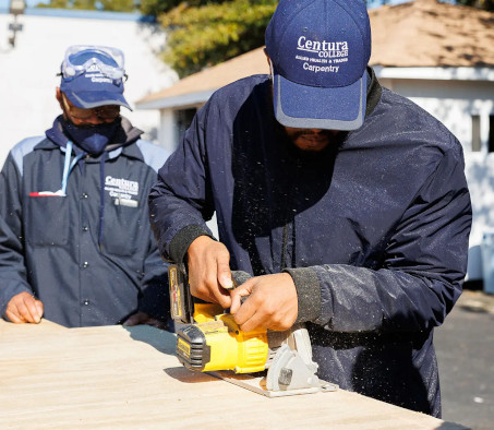 A carpentry student using a skill saw with an instructor watching