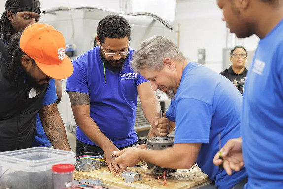 A construction electrician instructor working on a motor surrounded by students