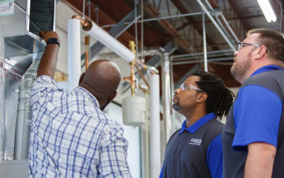 An HVAC instructor working on duct work with two students