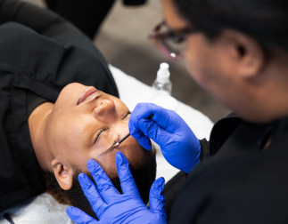 A master esthetician student practicing plucking eyebrows on another student
