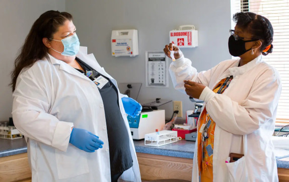 A medical assistant student next to an instructor that's demonstrating a blood draw