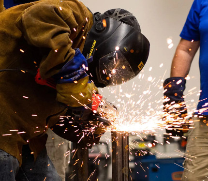 A Centura College welding program student using an angle grinder on a pipe