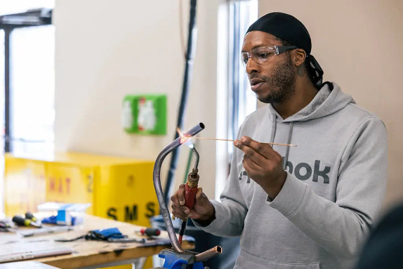 A welding student using a torch on a pipe