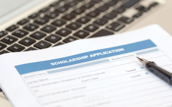 A paper scholarship application sitting on a desk by a keyboard