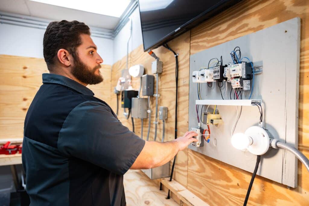A student practices wiring techniques on a circuit board as part of electrician license exam prep in a hands-on training lab at Centura College.